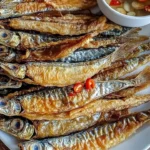 Crispy fried dried fish served on a plate with fresh herbs and lemon.