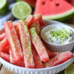 Bowl of watermelon fries served with coconut lime dip on a vibrant plate.